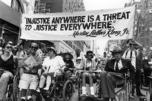 Disabled protesters underneath a banner that reads "Injustice anywhere is a threat to justice everywhere."