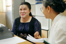 a close up of a smiling Asian woman and her colleague having a conversation in an office