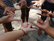 hands of different colored people standing in a circle, making the "I Love You" in American Sign Language