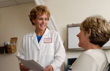 a middle-aged white woman with short blonde hair who is a doctor is smiling at a patient who is also a middle-aged white woman with short blonde hair