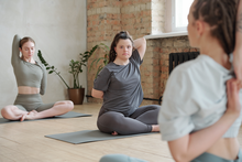 a young woman with Down Syndrome is doing a sitting yoga pose with two other young women