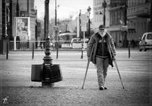 a black and white photograph of an older gentleman walking through a plaza using crutches
