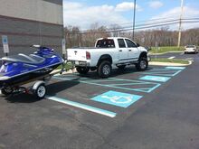 a white pick-up truck with a jetski on a trailer parked horizontally across multiple ADA parking spots