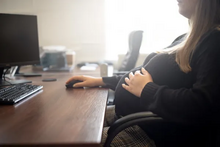a pregnant woman sitting at her computer, with her hand on her belly