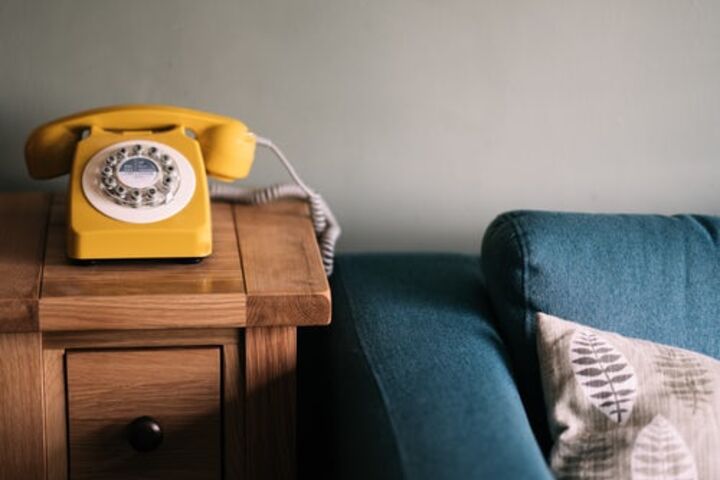 A yellow rotary phone on a table next to a blue sofa. 