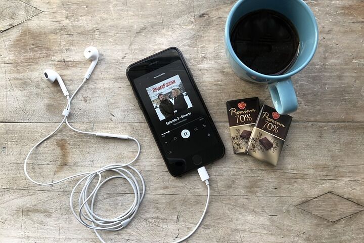 Smartphone with headphones, two chocolate bars and a cup of coffee.