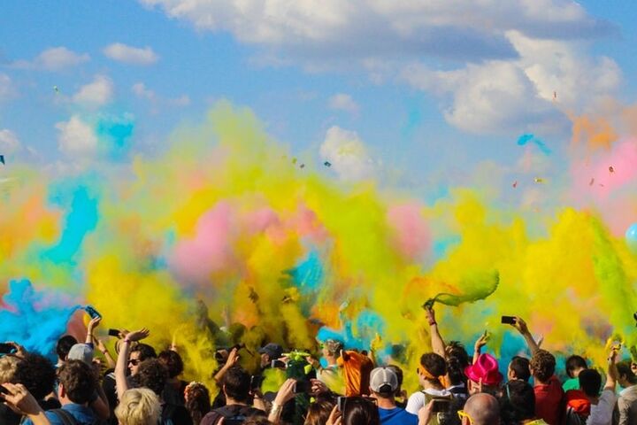 Crowd of people under a blue sky with yellow, blue, and pink colors above them