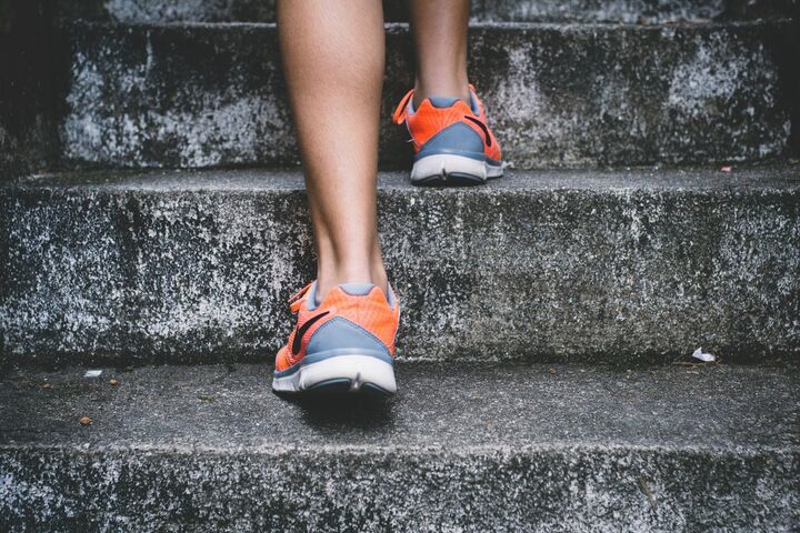 A close-up photo of a person’s orange shoes as he ascends rough concrete stairs.