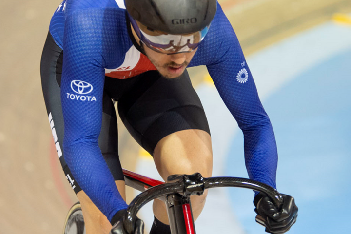Photo of Chris Murphy wearing a Team USA speedsuit slowly winding up speed at the top of a velodrome racing track.