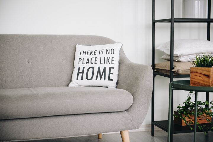 A pillow on a couch that reads, “There is no place like home.”