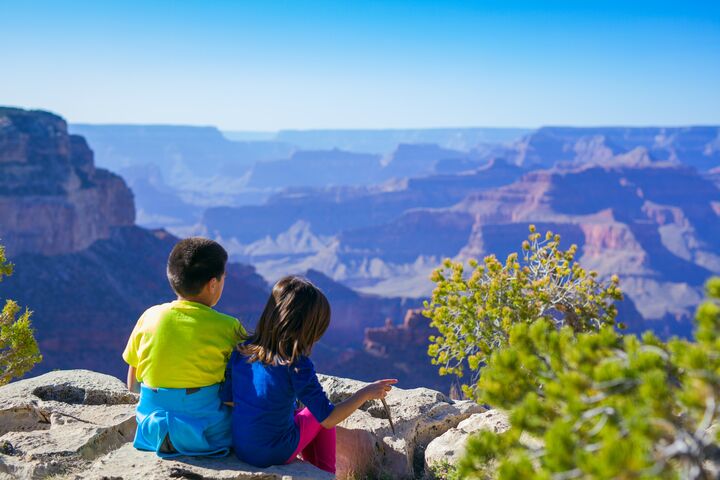 A brother and sister in colorful clothes enjoy the beautiful view of the Grand Canyon.