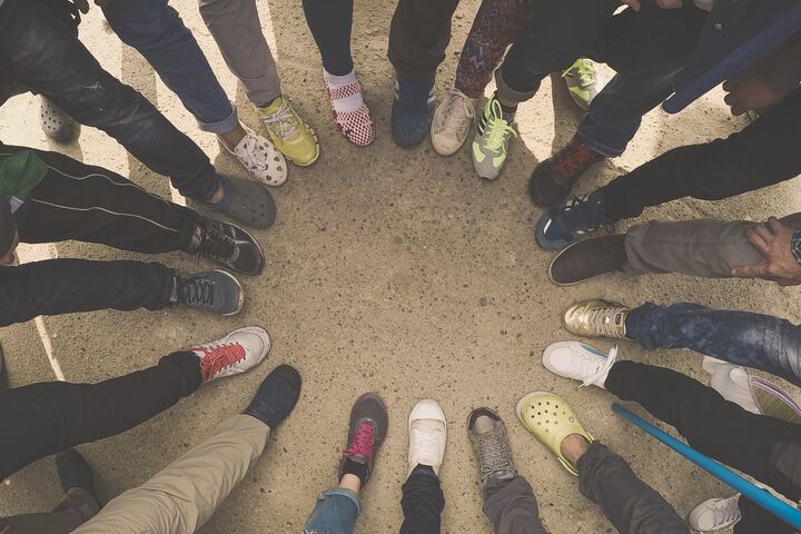 A circle is formed from a group of people all putting a foot down standing next to one another. Only the lower leg and shoes are pictured.