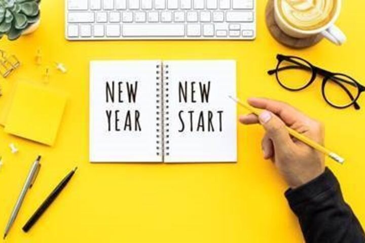 A hand holding a pencil that has written “new year - new start” in a notebook. 