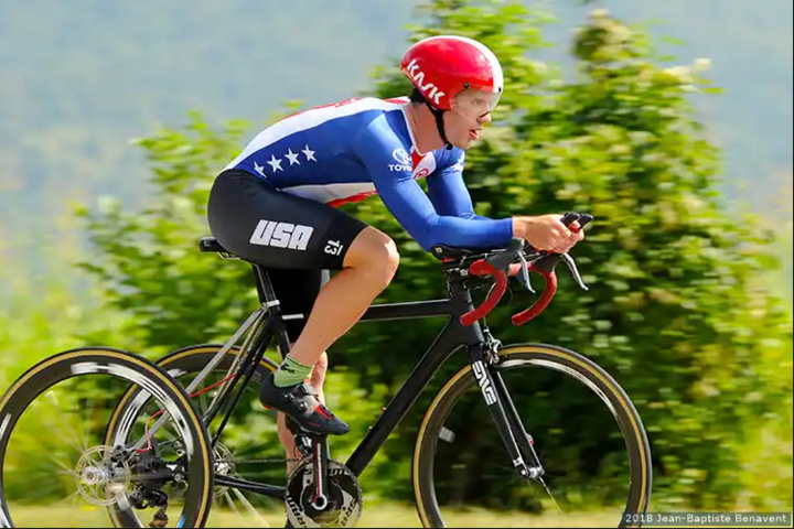 Ryan Boyle speeds on his trike in Team USA colors through a flat section of countryside meadow.