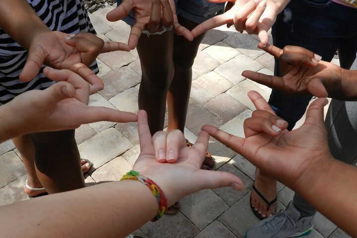 hands of different colored people standing in a circle, making the "I Love You" in American Sign Language
