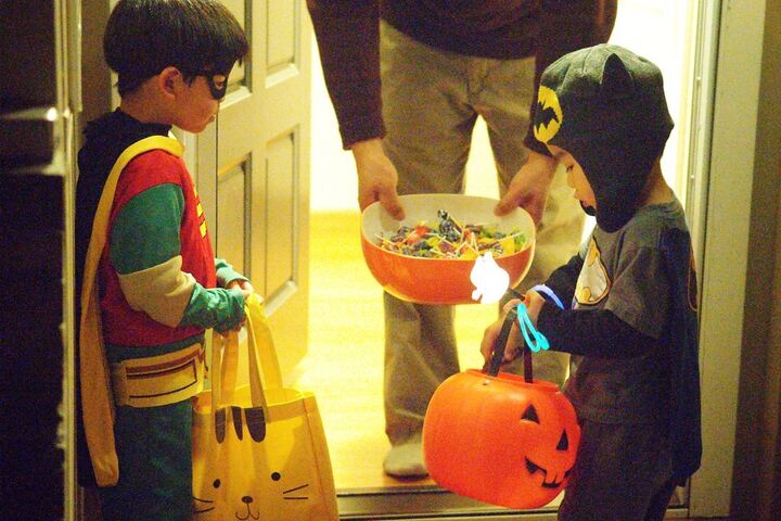 two children dressed in Halloween costumes are receiving Halloween candy at someone's front door