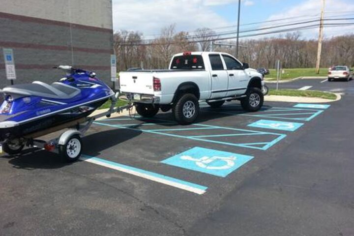 a white pick-up truck with a jetski on a trailer parked horizontally across multiple ADA parking spots