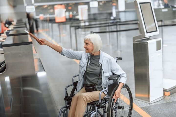 an older white woman in a wheelchair handing off her passport to an agent at the airport