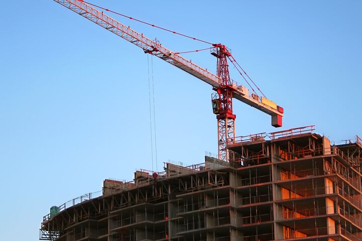 a construction crane sits on top of a tall incomplete building with a deep blue sky in the background