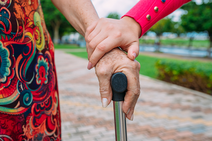 a close up of a younger woman's hand holding an older woman's hand that is on a cane