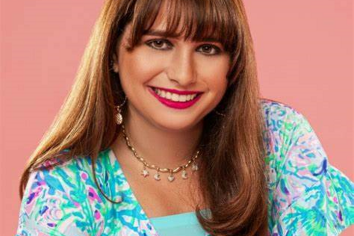 Haley Moss wearing a colorful blouse, smiles as she poses against a muted pink background.