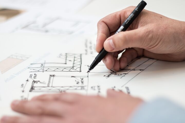 a close-up photo of an architect's hand holding a pen, sketching a layout on paper