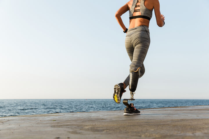 A woman with a prothetic lower leg running along a beach, a blue ocean composing the horizon