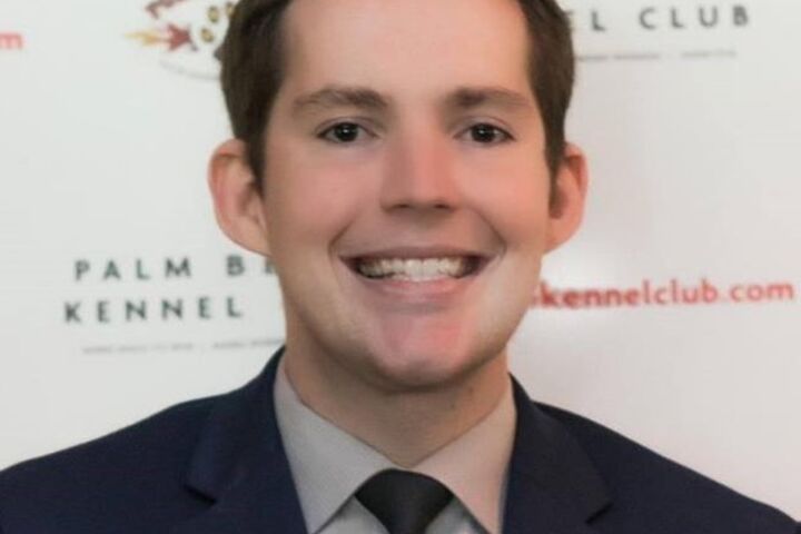 Dr. Kerry Magro smiling while wearing a black suit with gray shirt and blue tie. 