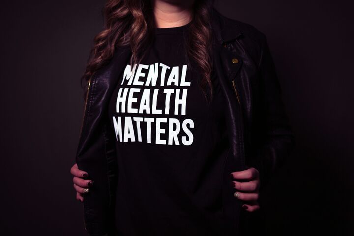 a brown hair woman holding open her black leather jacket and wearing a black tshirt with white words that says Mental Health Matters