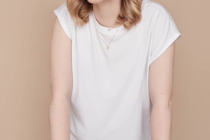 Rebecca Rosenberg, wearing a white tee and brown pants, leans against a brown leather chair.