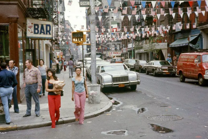 a vintage color photograph of a busy metropolitan street corner in the 1970s, with a vertical curb surrounding the sidewalk corner radius