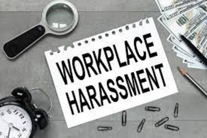 a magnifying glass, a black clock, black paperclips, money and pens scattered around a piece of paper that has "WORKPLACE HARASSMENT" in black text