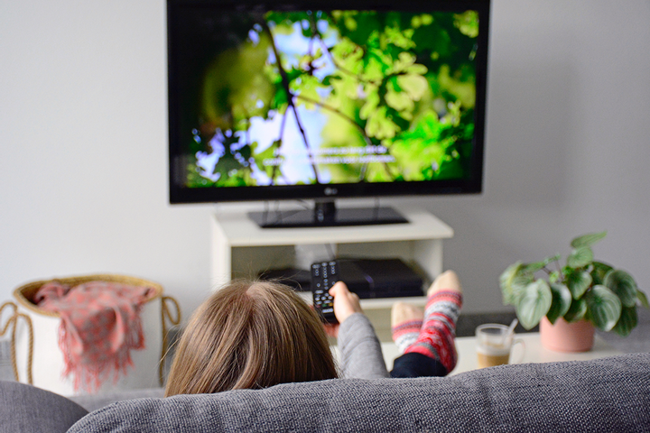 a woman is lounging on a gray couch watching a show with audio description text on the tv screen