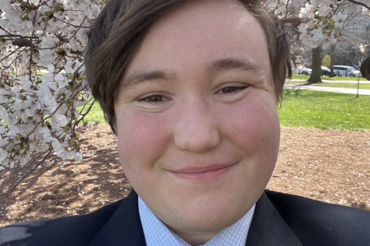 Emmett Lockwood smiles while wearing a suit and tie against a tree with white flowers.