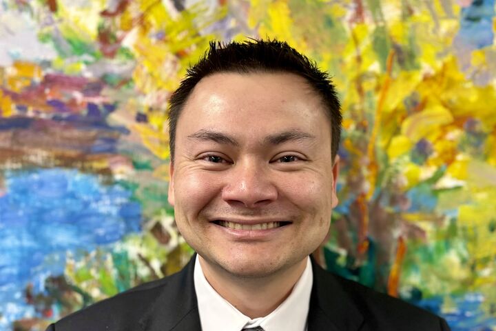 Thomas Martin in a patterned tie and black suit smiles against a colorful painted background.