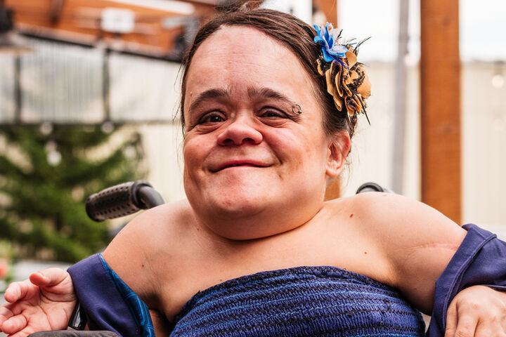 Gaelynn Lea wears a navy blue dress and has flowers in her hair while she poses for a photograph.
