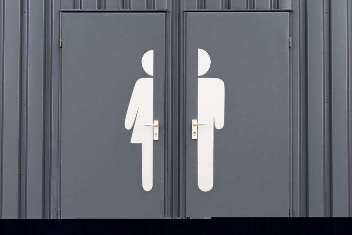 a pair of gray restroom doors, one labeled with a large pictogram of a woman and the other of a man