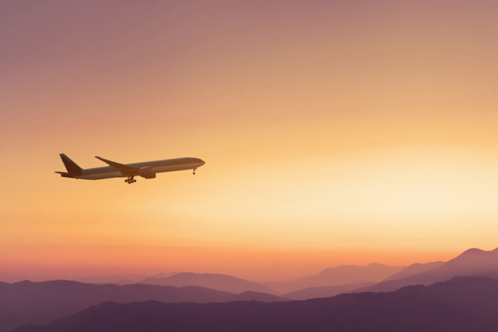 an airplane flying in the sky with purple mountains in the background at sunset
