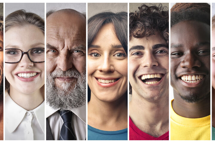 A close-up photo of 7 people of different sexes, ages, and ethnicities, all smiling side by side.