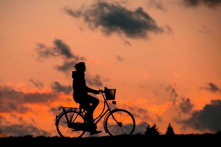 Silhouette of a person on a bike, with a sunset background. 
