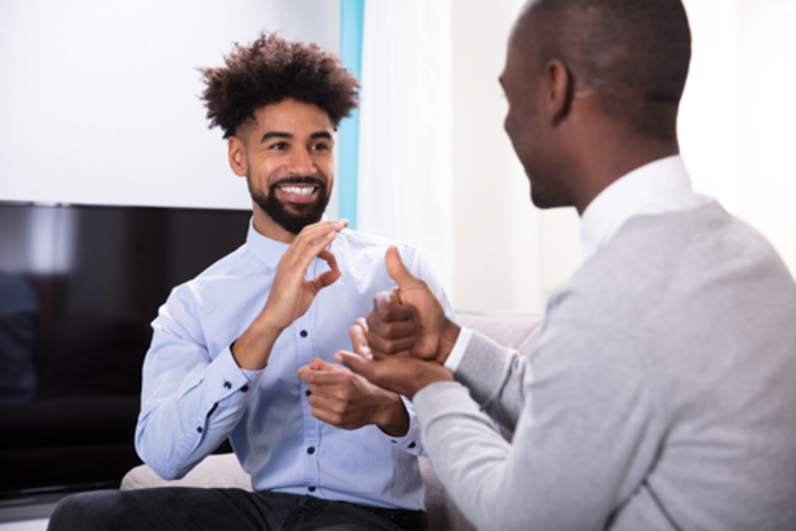 a black man wearing a blue button up is signing to another black man wearing a grey cardigan