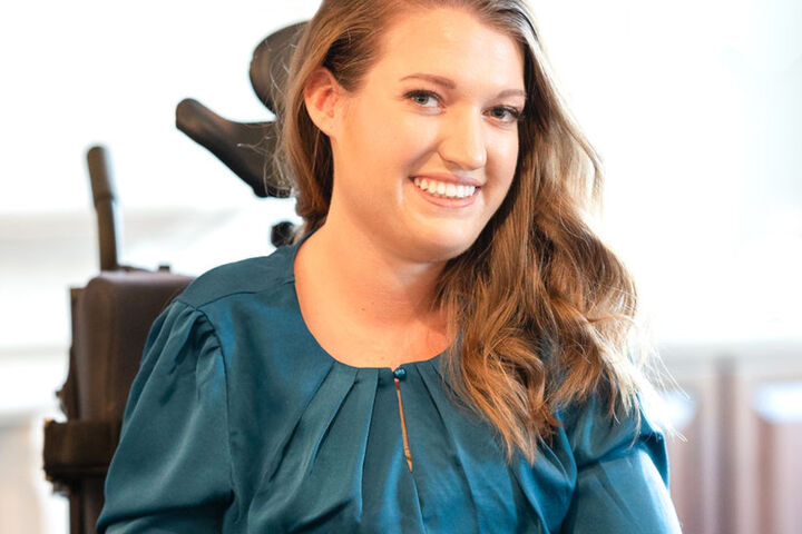 Annie Heathcote wears a blue satin long sleeve blouse and her light brown hair is on her left shoulder.