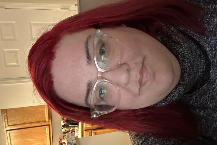 Kaeia Perez wears clear frame glasses and bright red hair.