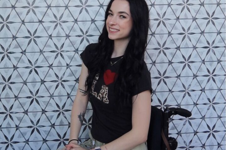 Bella Mohn smiles in her wheelchair against an abstract background.