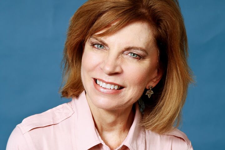 Gail Nehls wears a light pink button down blouse, a smile, and her short light brown hair. 