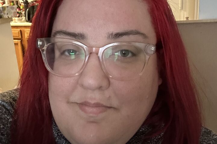 Kaeia Perez wears clear frame glasses and bright red hair.