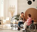 Two women meeting in hotel lobby dressed business casual, one in wheelchair