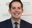 Dr. Kerry Magro smiling while wearing a black suit with gray shirt and blue tie. 