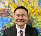 Thomas Martin in a patterned tie and black suit smiles against a colorful painted background.