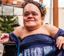 Gaelynn Lea wears a navy blue dress and has flowers in her hair while she poses for a photograph.